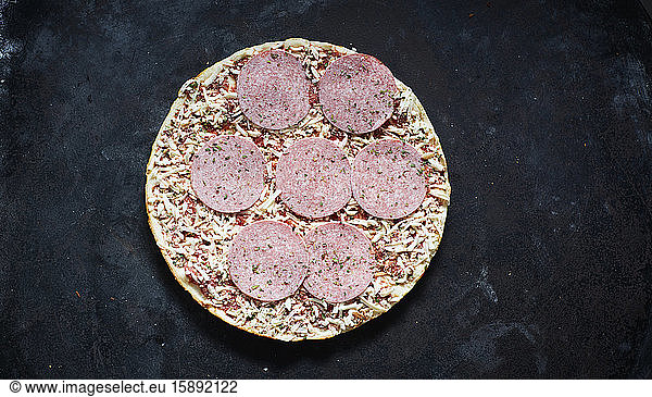 Frozen pizza with salami and grated cheese