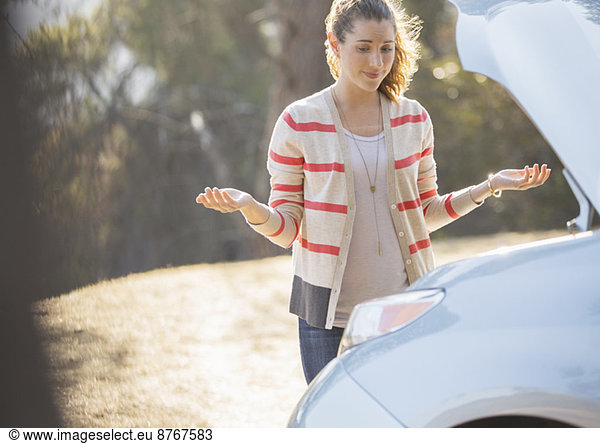 Frustrated woman looking at car engine at roadside
