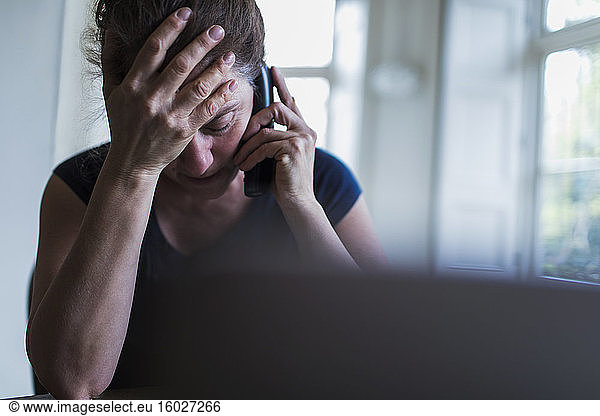 Frustrated woman talking on telephone at laptop