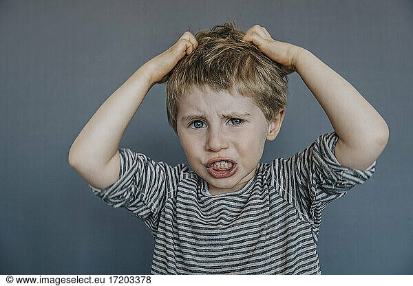Frustrierter Junge kratzt sich am Kopf vor grauem Hintergrund