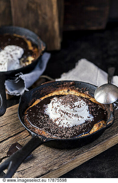 Frying pan with chocolate chip cookies covered with ganache topping and whipped cream
