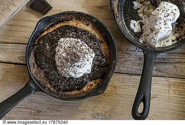 Frying pans with chocolate chip cookies covered with ganache topping and whipped cream