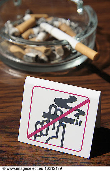 Full ashtray behind no smoking sign  close-up