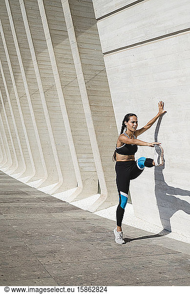 Full body of female athlete stretching legs against concrete wall
