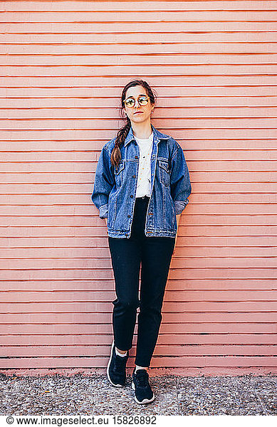 Full body portrait of an attractive young woman on a pink brick wall. Vertical image