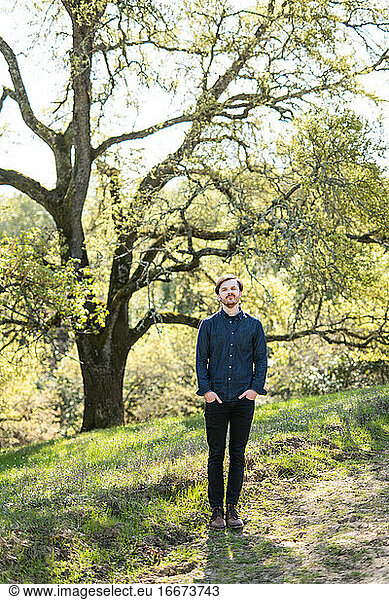Full body portrait of man in casual clothes in front of Oak tree