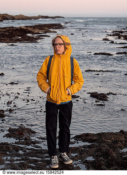Full body portrait of tween standing on rocky shore at sunset