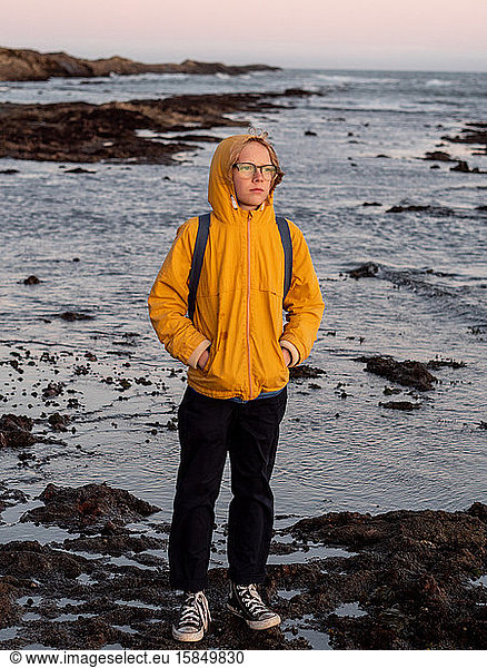 Full body portrait of tween standing on rocky shore at sunset