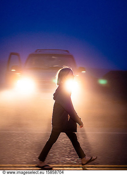 Full body profile shot of tween walking on roadway in front of lights