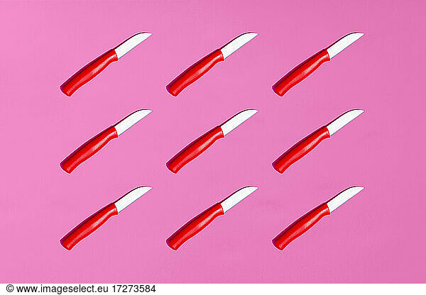 Full frame of table knives on pink background