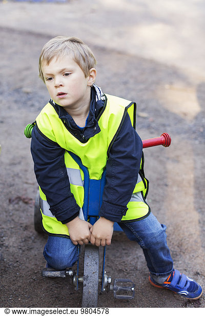 Full length of boy in reflective jacket sitting on tricycle