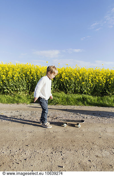 Full length of boy preparing to skateboard on dirt road at oilseed rape field