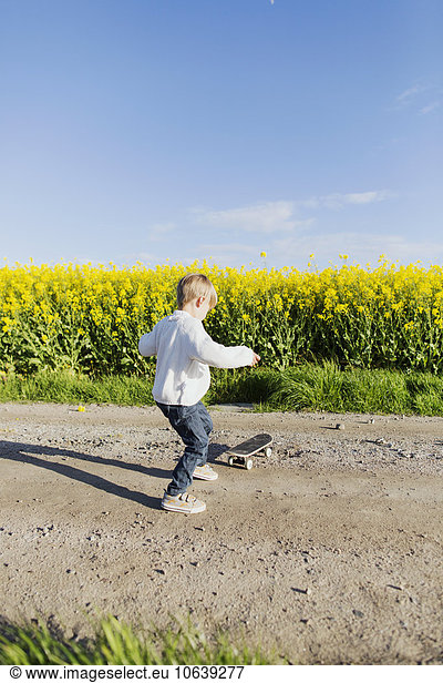 Full length of boy preparing to skateboard on dirt road at oilseed rape field