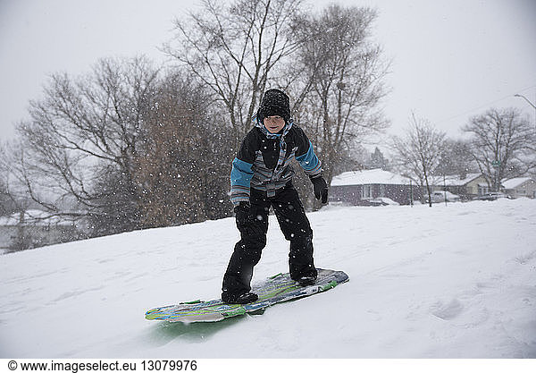 Full length of boy tobogganing on snow during snowfall