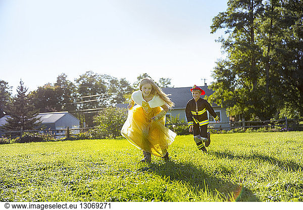 Full length of brother and sister in Halloween costumes running on field