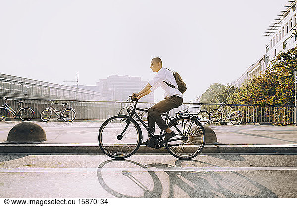 Full length of businessman riding bicycle on street in city against sky