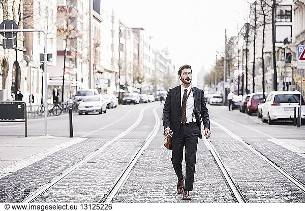 Full length of businessman walking by railroad tracks in city