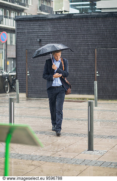 Full length of businessman walking on sidewalk during rainy season