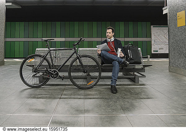 Full length of businessman with document sitting on bench by bicycle at subway station in Frankfurt  Germany