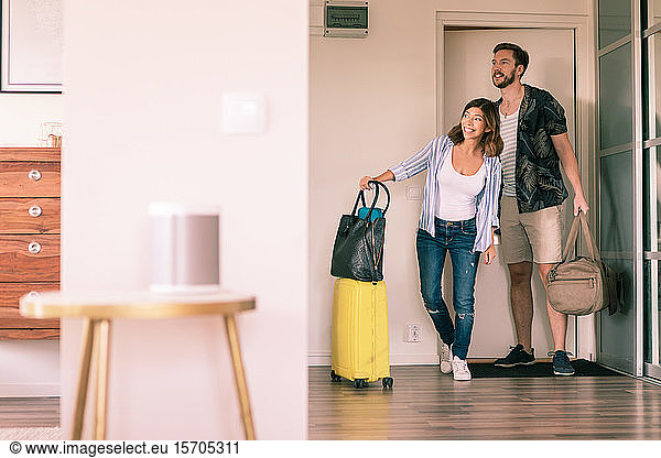 Full length of couple with luggage looking around in apartment while standing at doorway