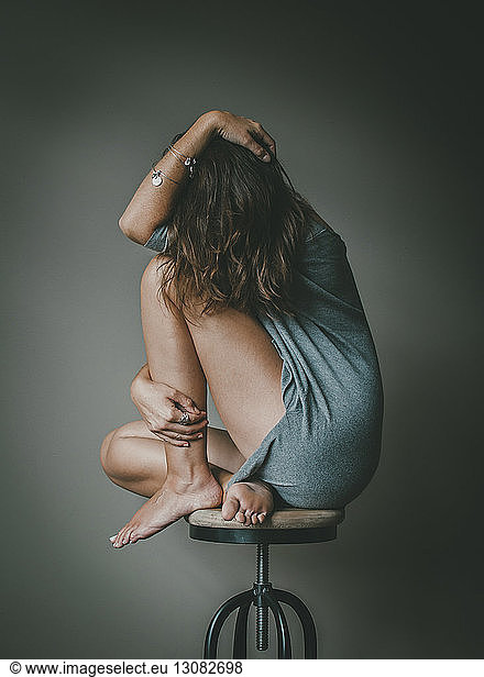 Full length of depressed woman with obscured face sitting on stool against wall