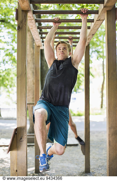 Full length of determined man hanging on monkey bars at outdoor gym