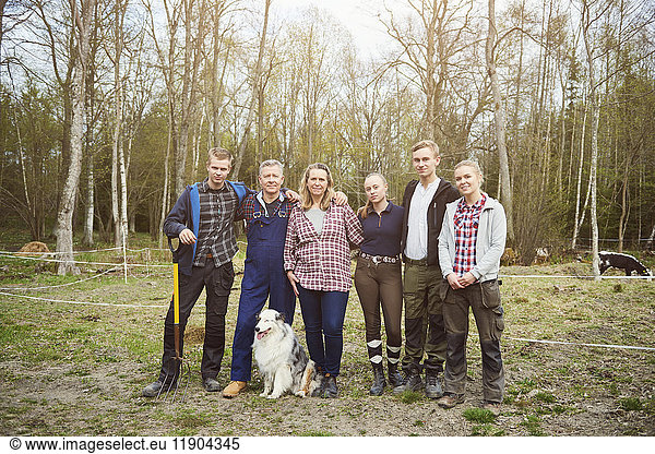 Full length of farmer with family standing on field against trees