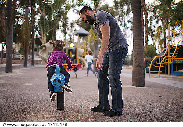 Full length of father looking at daughter playing on outdoor play equipment at playground