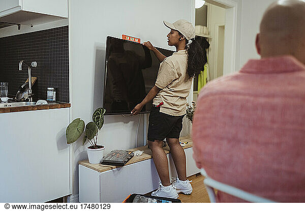 Full length of female maintenance engineer installing television set on wall in living room