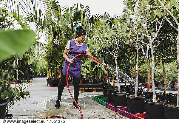 Full length of female owner watering potted plants at nursery