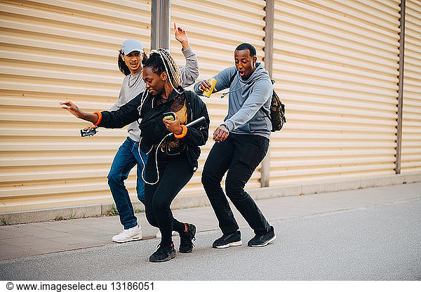Full length of friends dancing on sidewalk by shutter in city