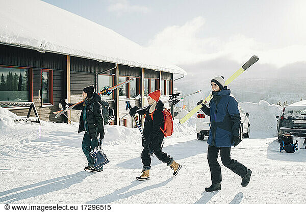 Full length of friends walking with skis at tourist resort during sunny day