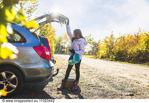 Full length of girl looking into open car trunk in countryside