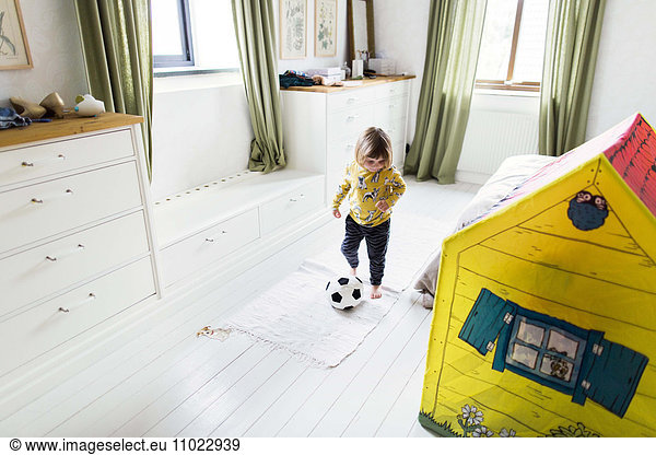 Full length of girl playing with soccer ball in bedroom