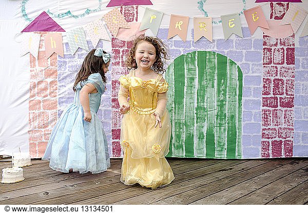 Full length of girls playing on floorboard against castle painting during princess party
