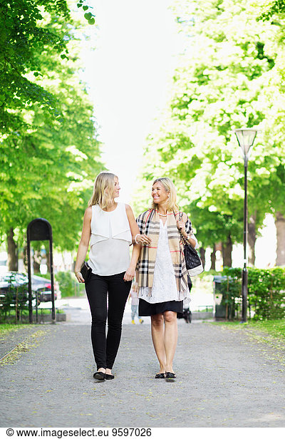 Full length of happy female friends communicating walking on garden path