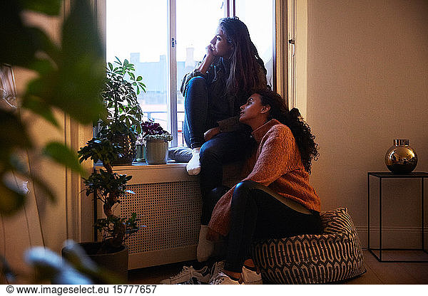 Full length of lesbian couple sitting by window at rental apartment during vacation