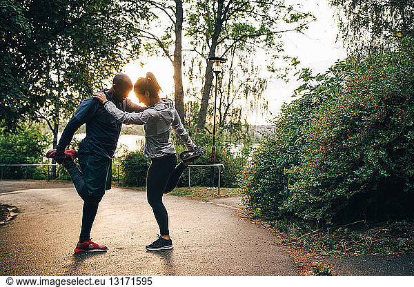 Full length of male and female athletes stretching legs while standing on road in park