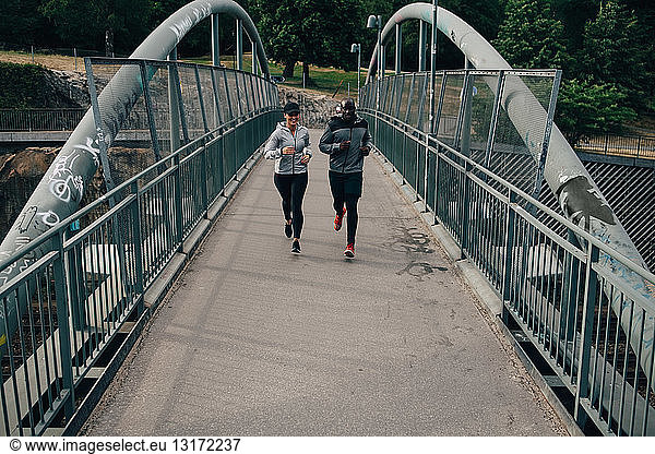 Full length of male and female friends jogging on footbridge in city