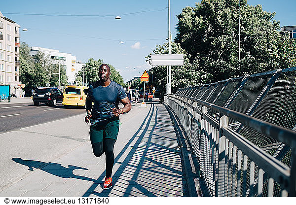 Full length of male athlete jogging on sidewalk at bridge in city