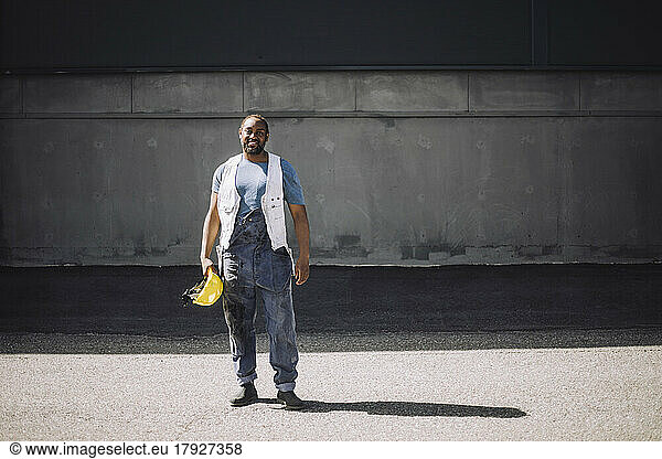 Full length of male construction worker with hardhat standing on road during sunny day