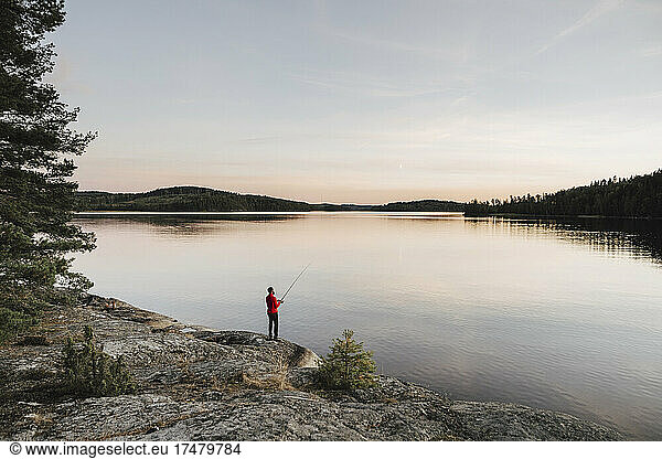 Full length of man fishing at lakeshore during sunset