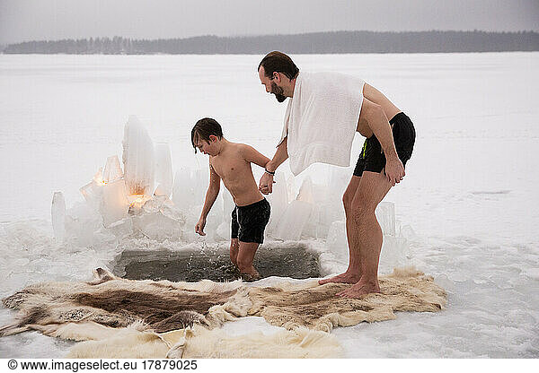 Full length of man holding hand of son taking ice bath at frozen lake