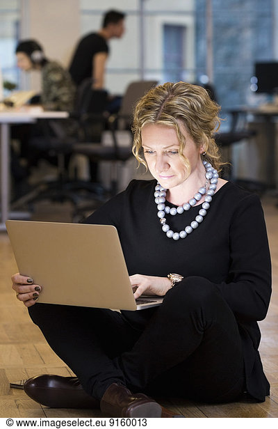 Full length of mature businesswoman using laptop while sitting on floor at office