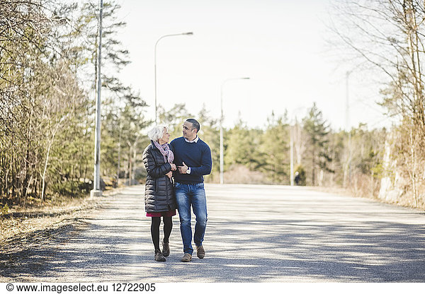 Full length of mature man walking arm in arm with mother on road