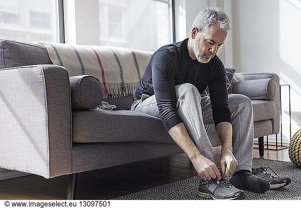Full length of mature man wearing sports shoe at home