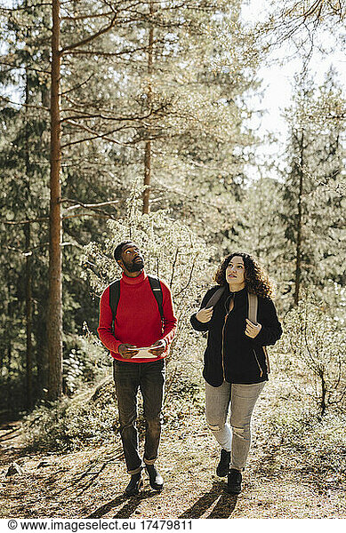 Full length of multiracial couple walking in forest on sunny day