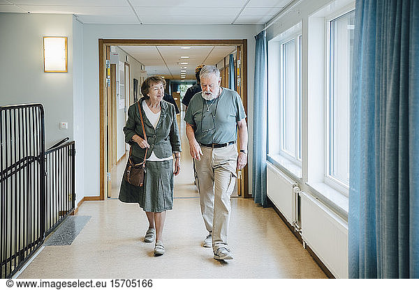 Full length of senior couple walking in alley at elderly nursing home