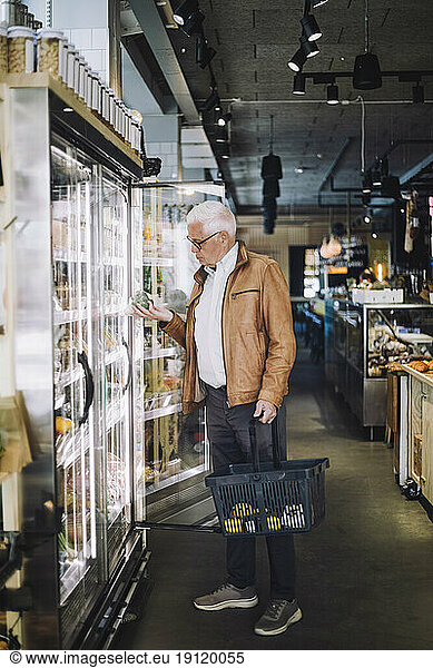 Full length of senior man analyzing organic vegetable at grocery store