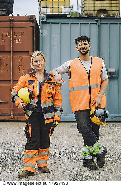Full length of smile male and female construction workers in reflective clothing standing at site